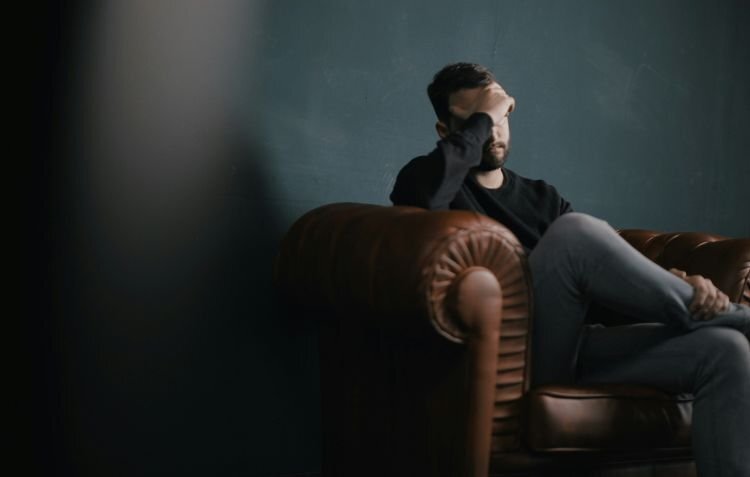 man sitting on leather couch holding forehead