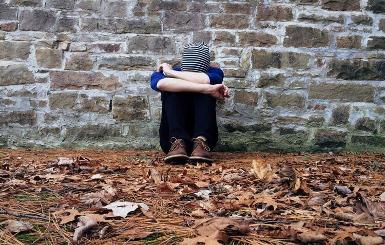 boy sitting on ground against a wall with head on knees